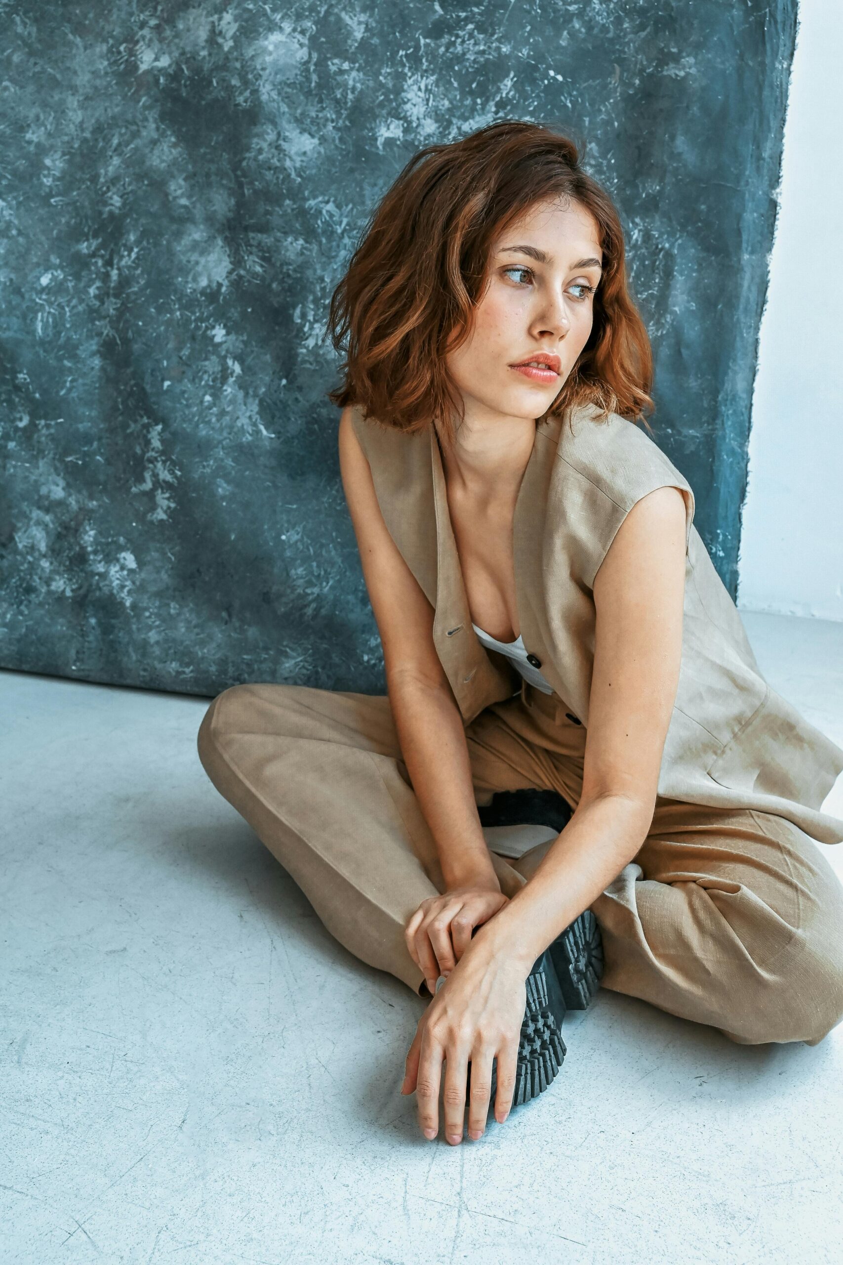 Stylish woman in beige clothing posing thoughtfully against a textured backdrop.