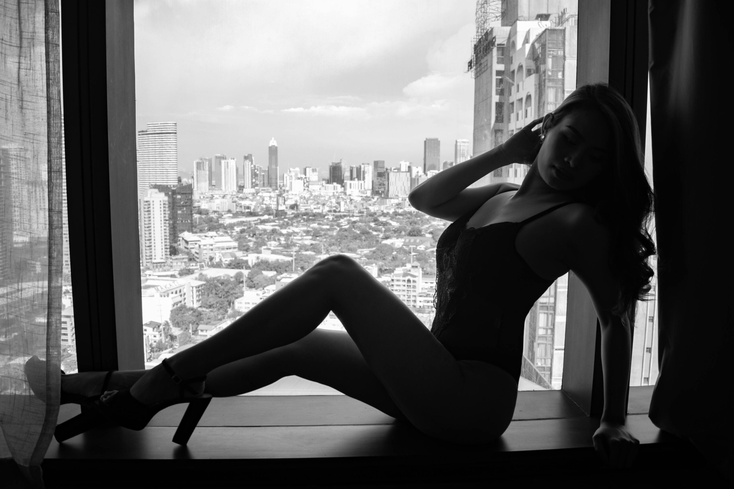 Black and white silhouette of a woman posing by a city window, creating a dramatic scene.